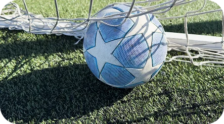 Un ballon de football avec des motifs d'étoiles bleues repose au fond des filets d'un but sur un terrain synthétique