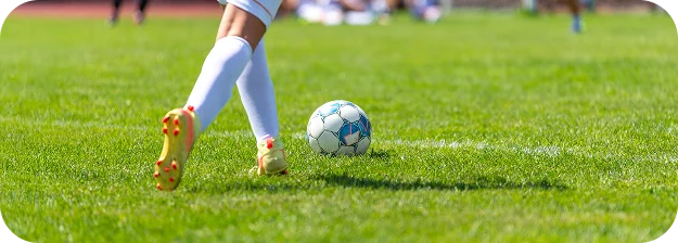 Vue rapprochée des jambes d'un joueur de football en chaussettes blanches et crampons jaunes menant le ballon sur une pelouse verte